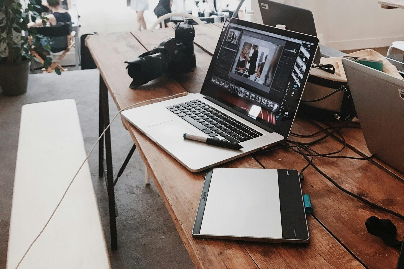 A bright, modern workspace featuring laptops, a camera, and a drawing tablet in an indoor office.